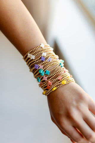 A person's wrist wearing multiple gold-colored bracelets with different patterns and decorations by enewton 