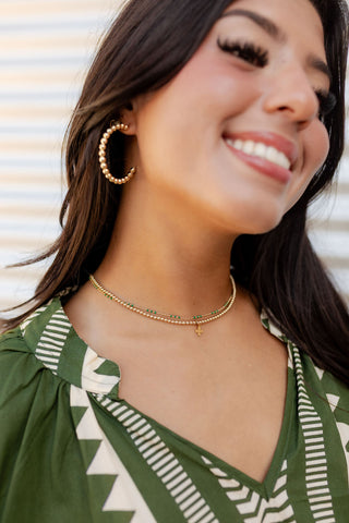 Woman wearing gold hoop earrings and necklaces in a natural setting by enewton